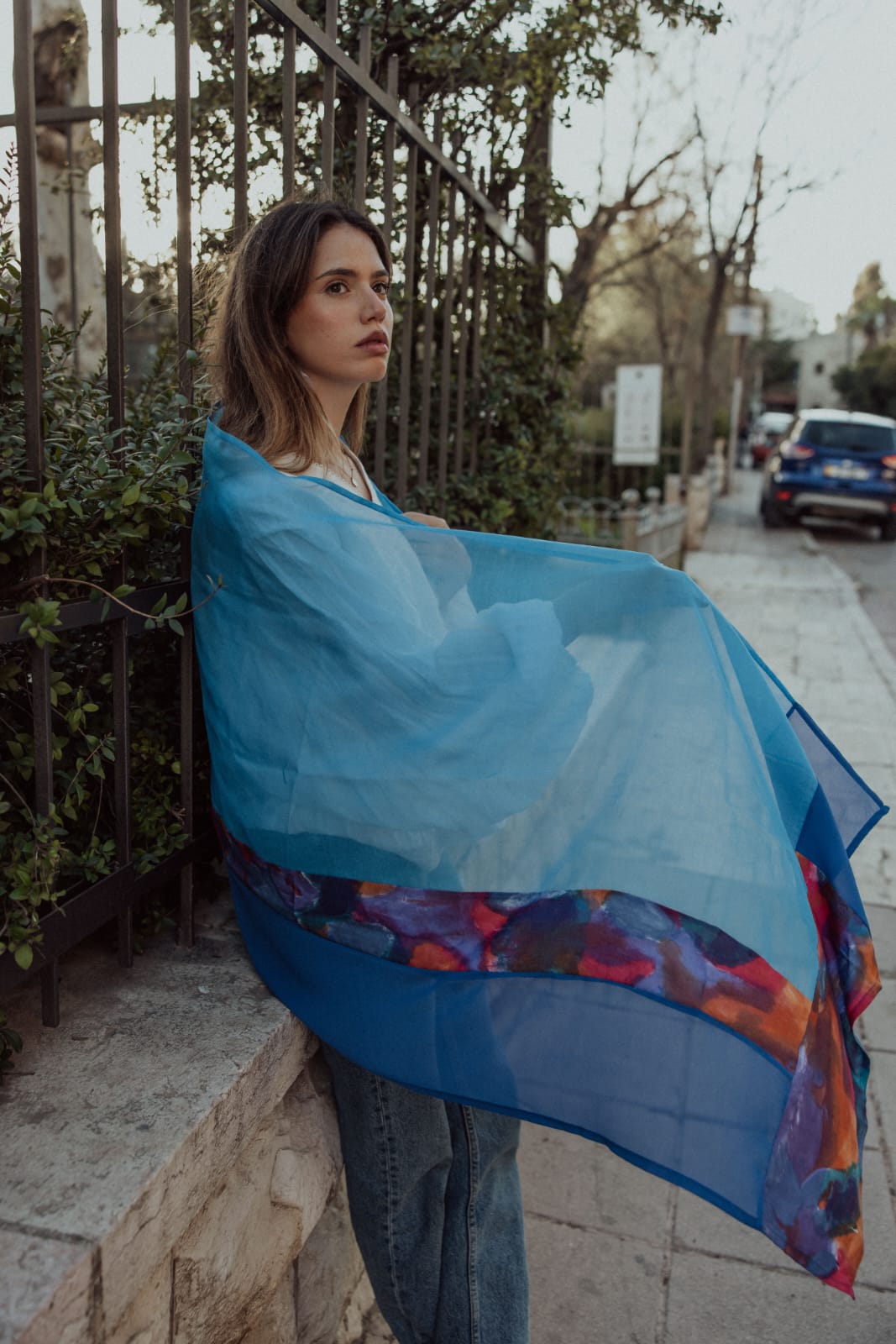 Sheer blue scarf with hand-painted abstract border, worn outdoors
